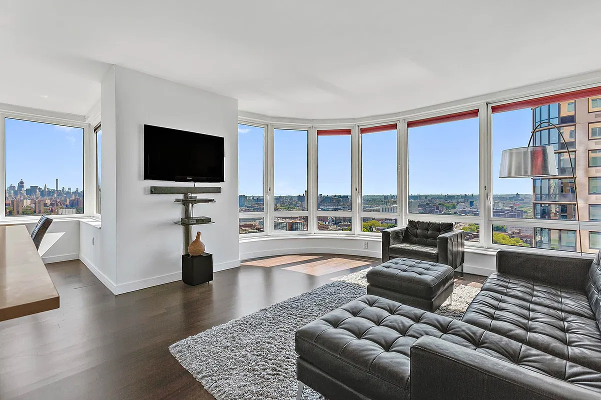 Corner living room with curved floor-to-ceiling windows, black leather sofa and Brooklyn skyline views