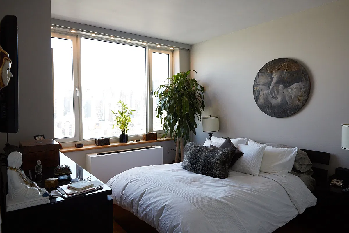 Thumbnail: Bedroom with white bedding, potted plant and large windows overlooking Midtown towers