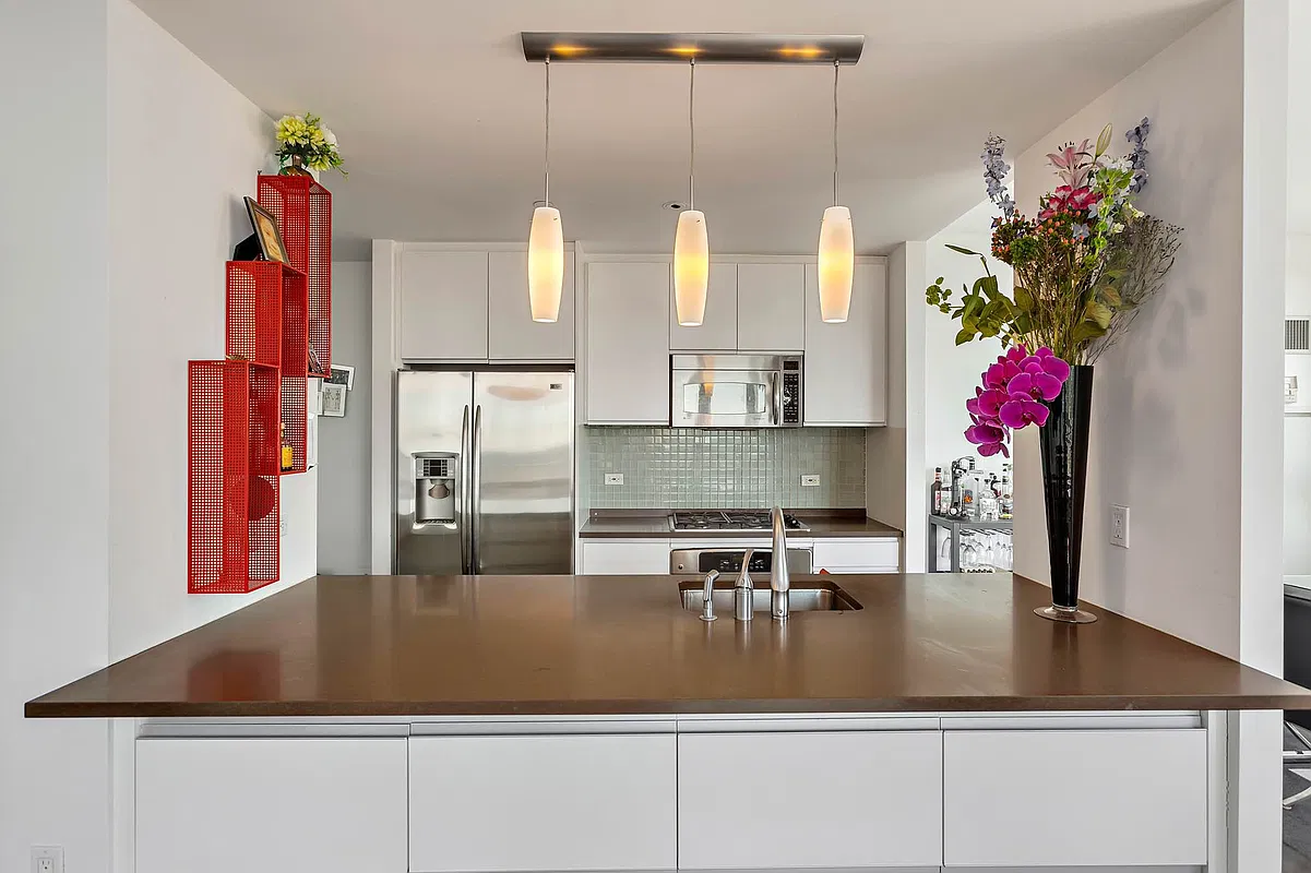 Thumbnail: Open kitchen with white cabinetry, stainless steel refrigerator, microwave and pendant lights over a peninsula