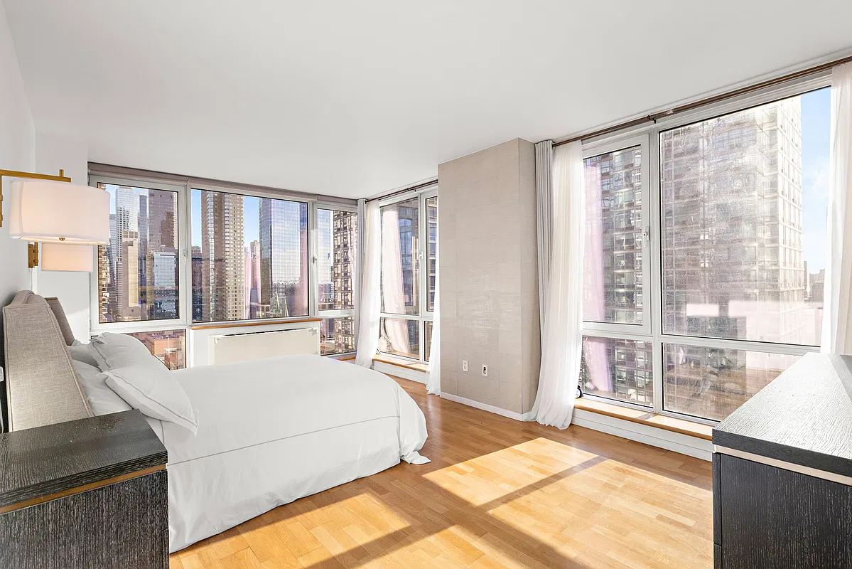 Thumbnail: Sunlit bedroom with white bedding, sheer curtains and wraparound windows onto the skyline