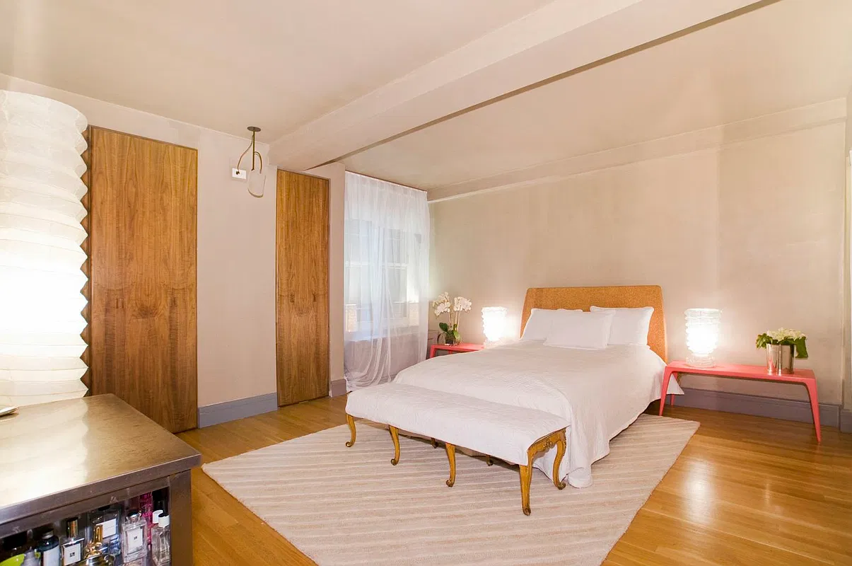 Thumbnail: Bedroom with walnut closet doors, upholstered bed, coral nightstands and sheer-curtained window