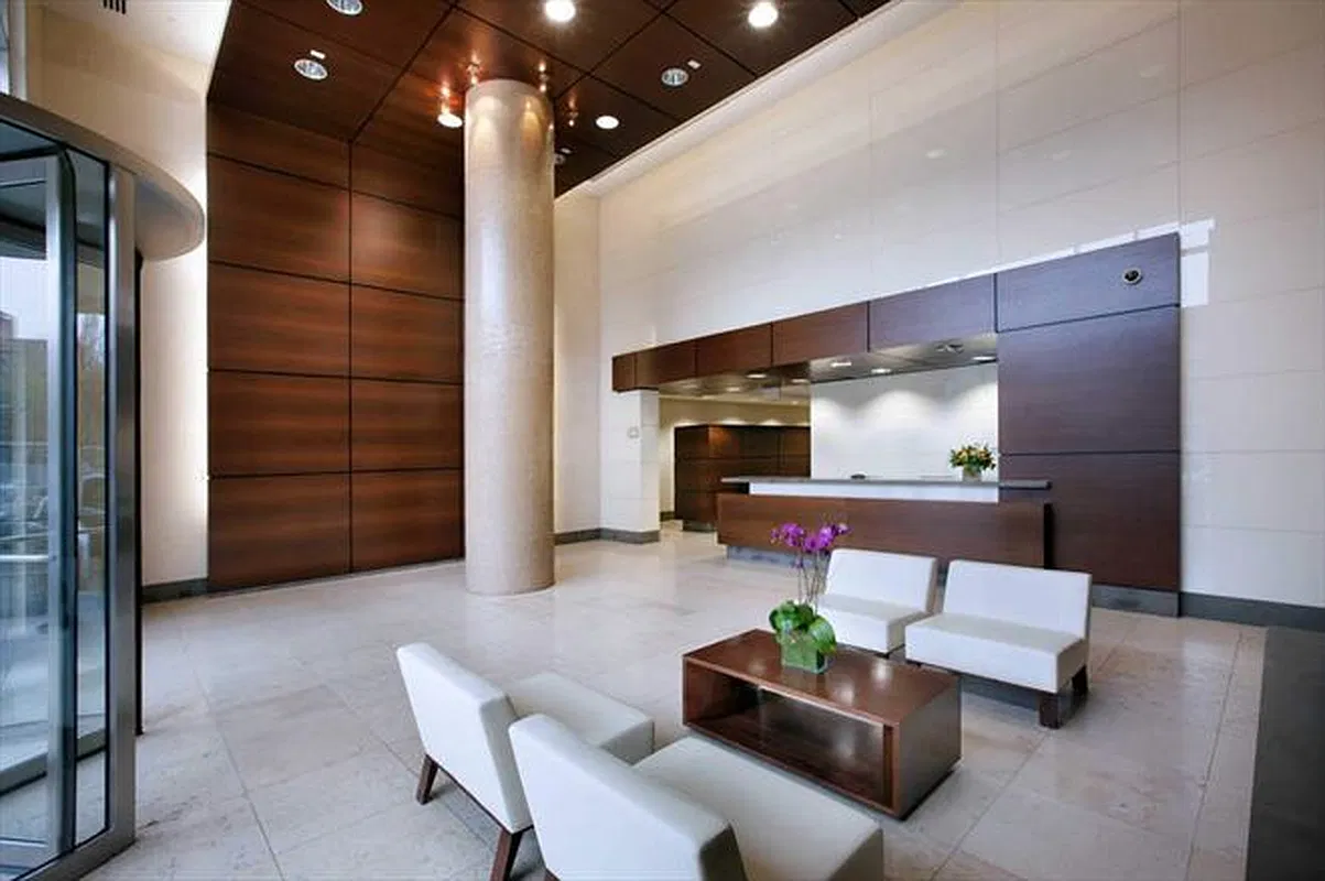 Thumbnail: Building lobby with wood-paneled walls, stone column, concierge desk and white lounge chairs