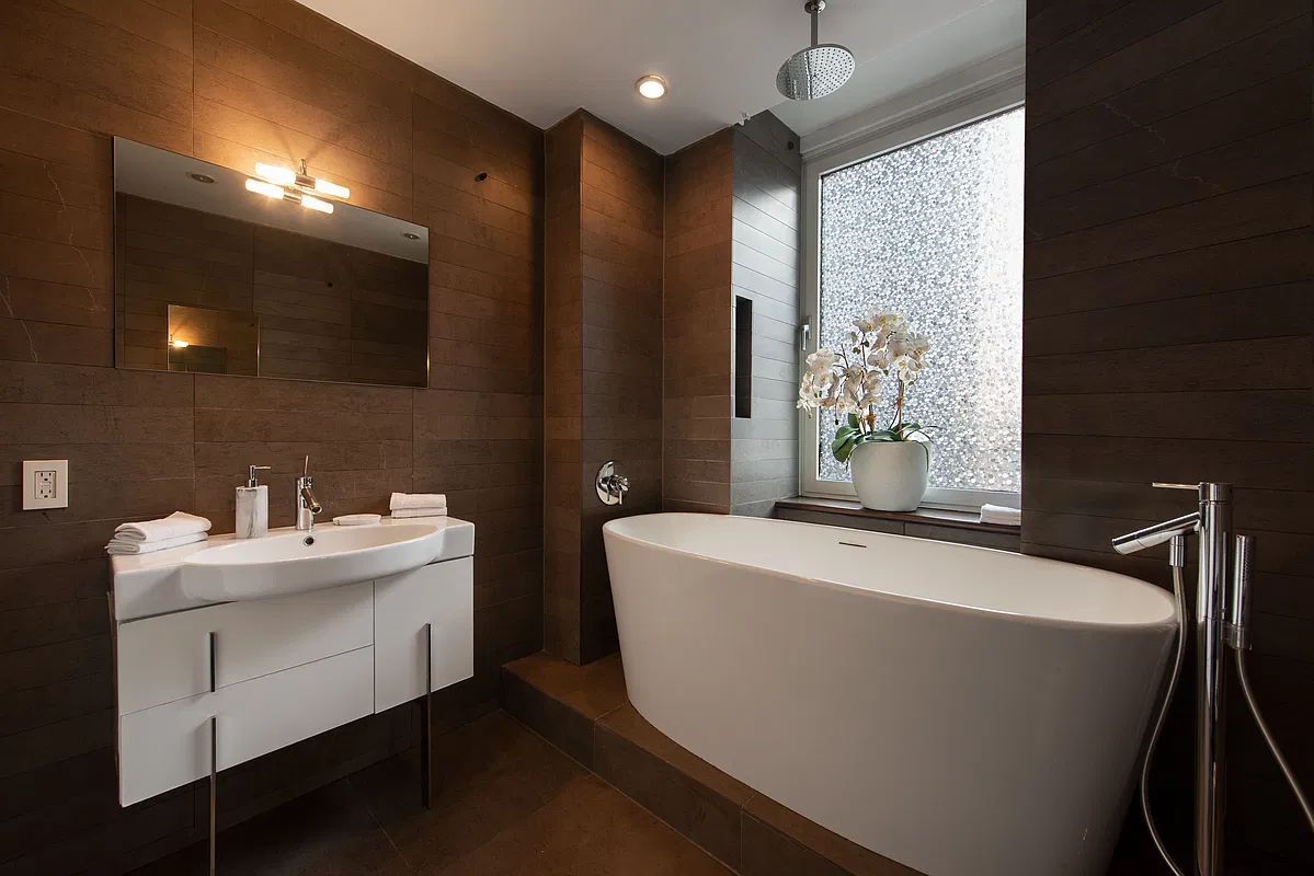 Thumbnail: Bathroom with freestanding soaking tub, rain shower, white vanity and dark tile walls